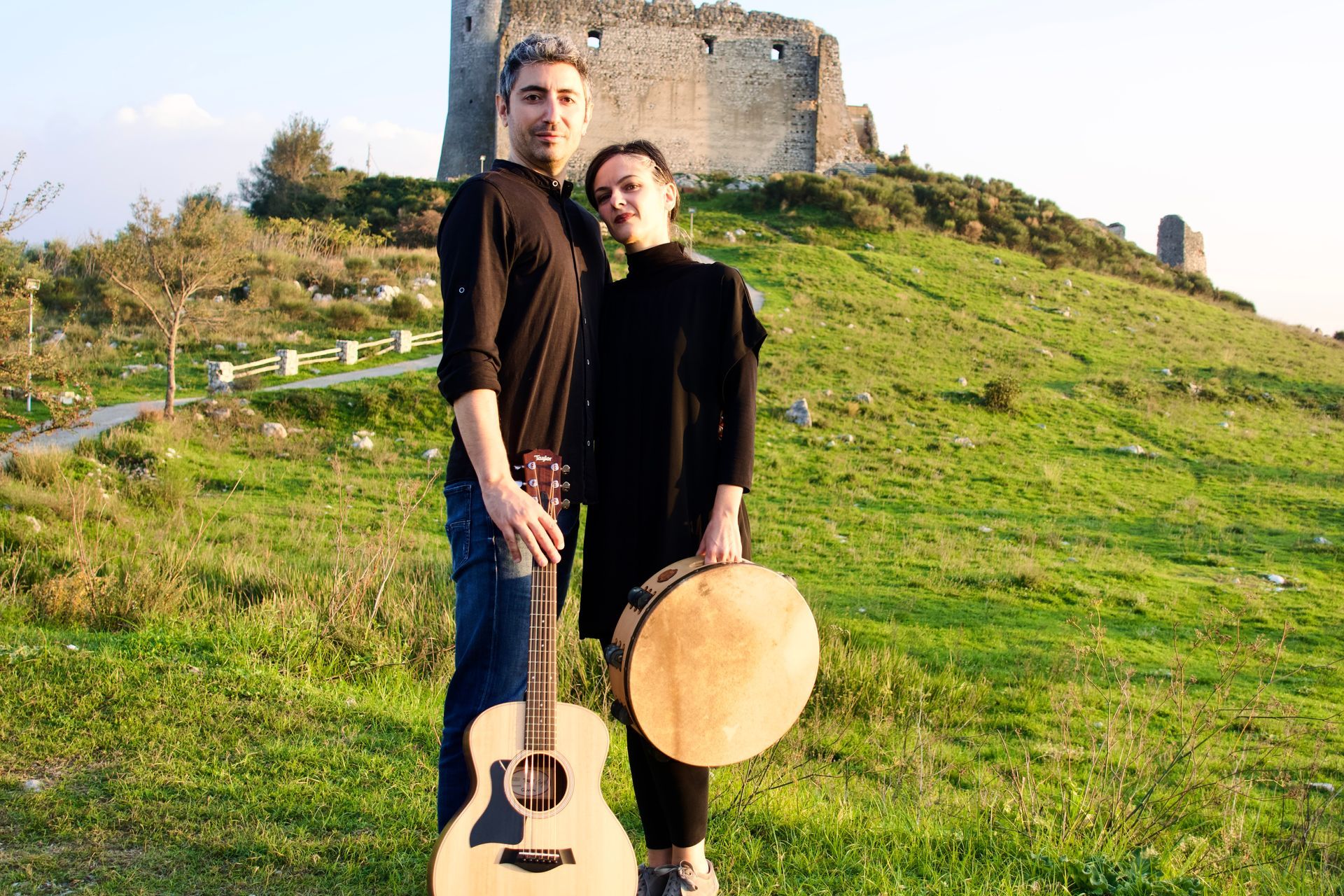Un uomo e una donna sono in piedi in un campo con una chitarra e un tamburo.