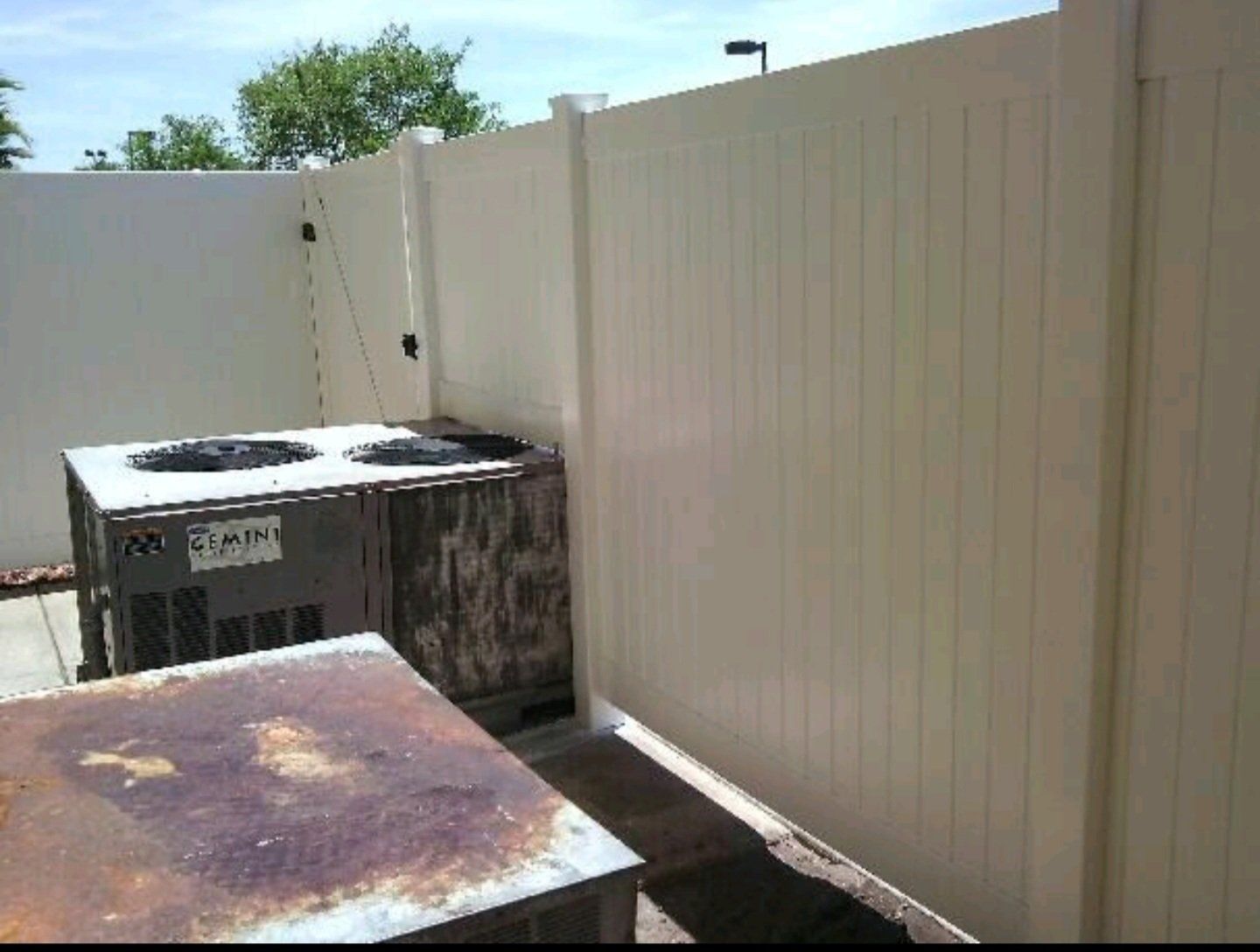 two air conditioners are behind a white fence