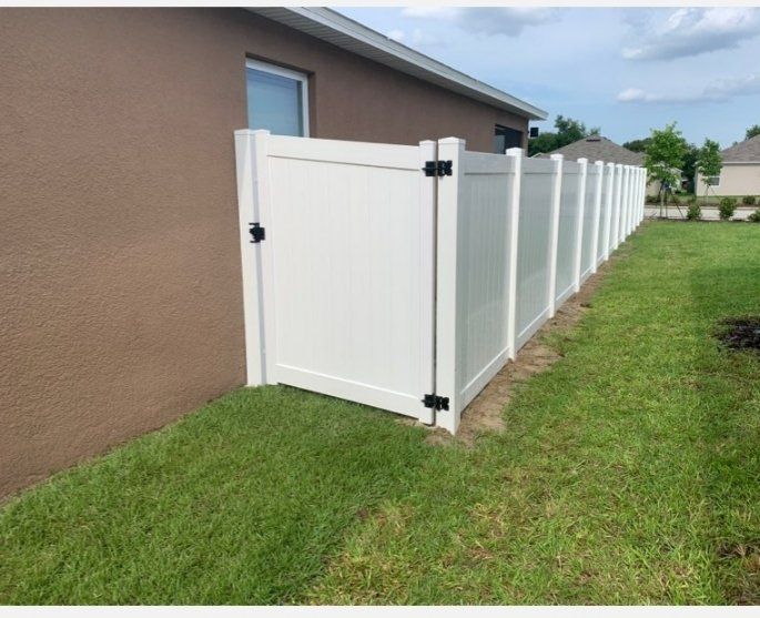 a white fence is sitting in the grass next to a brown house .