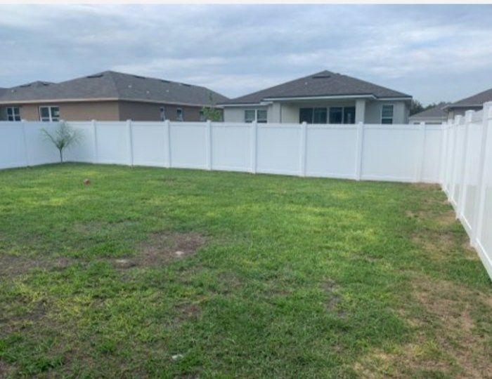 a white fence surrounds a lush green yard with houses in the background .