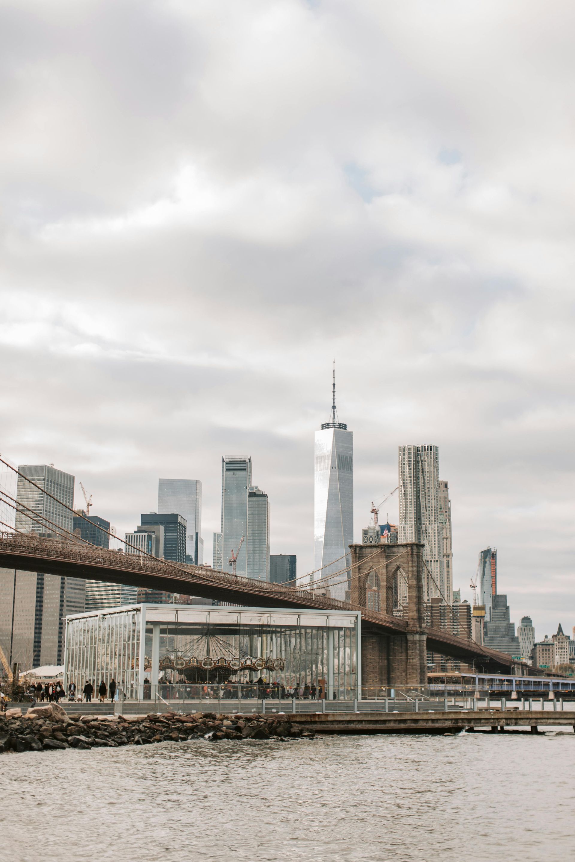 Brooklyn Bridge with NYC skyline under a cloudy sky.
