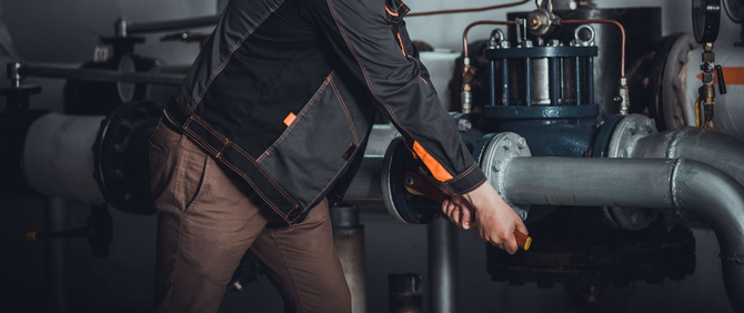 Person in work clothes adjusting a pipe in an industrial setting.