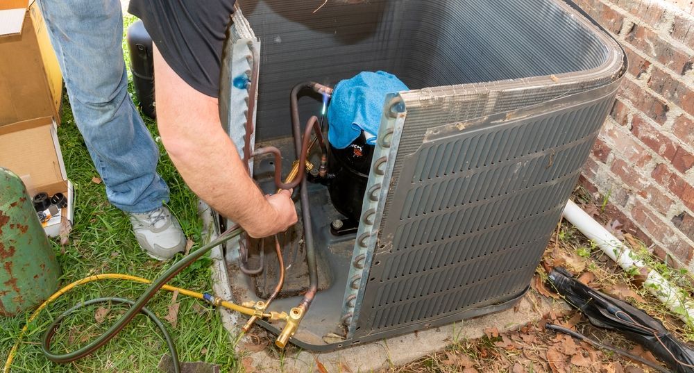 HVAC technician repairing an air conditioning unit outside, connecting hoses.