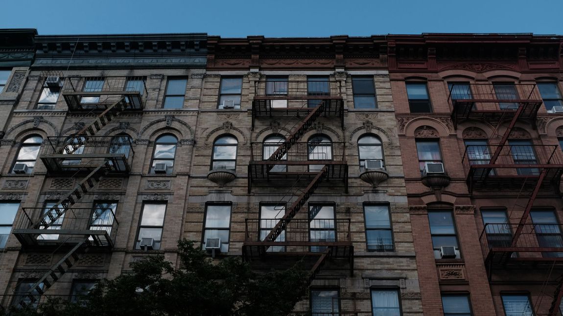 Row of old brick buildings with fire escapes and windows against a blue sky.