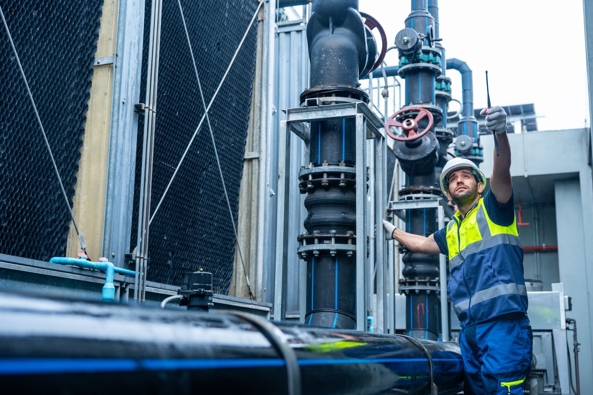 Man in safety gear inspecting industrial pipes outside.