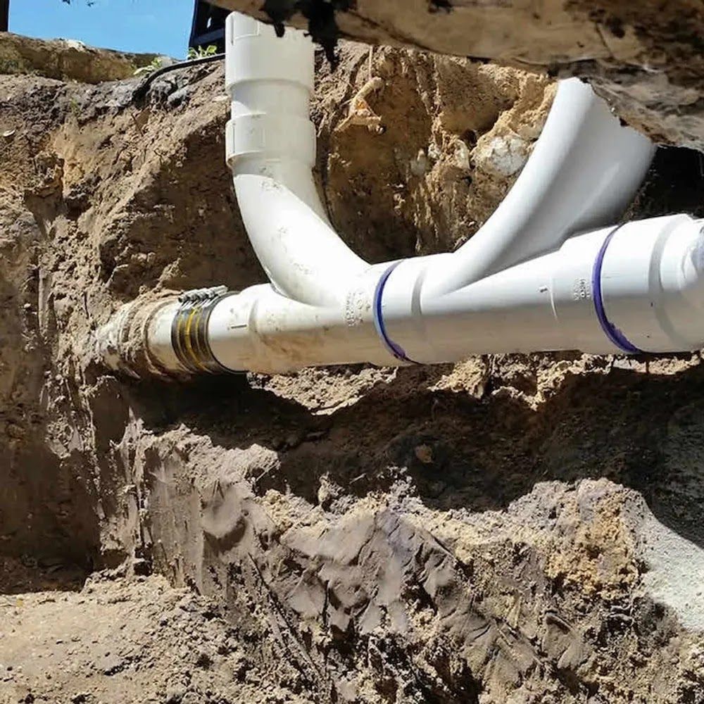 White PVC pipes connected in an earthen trench, showing a plumbing repair.