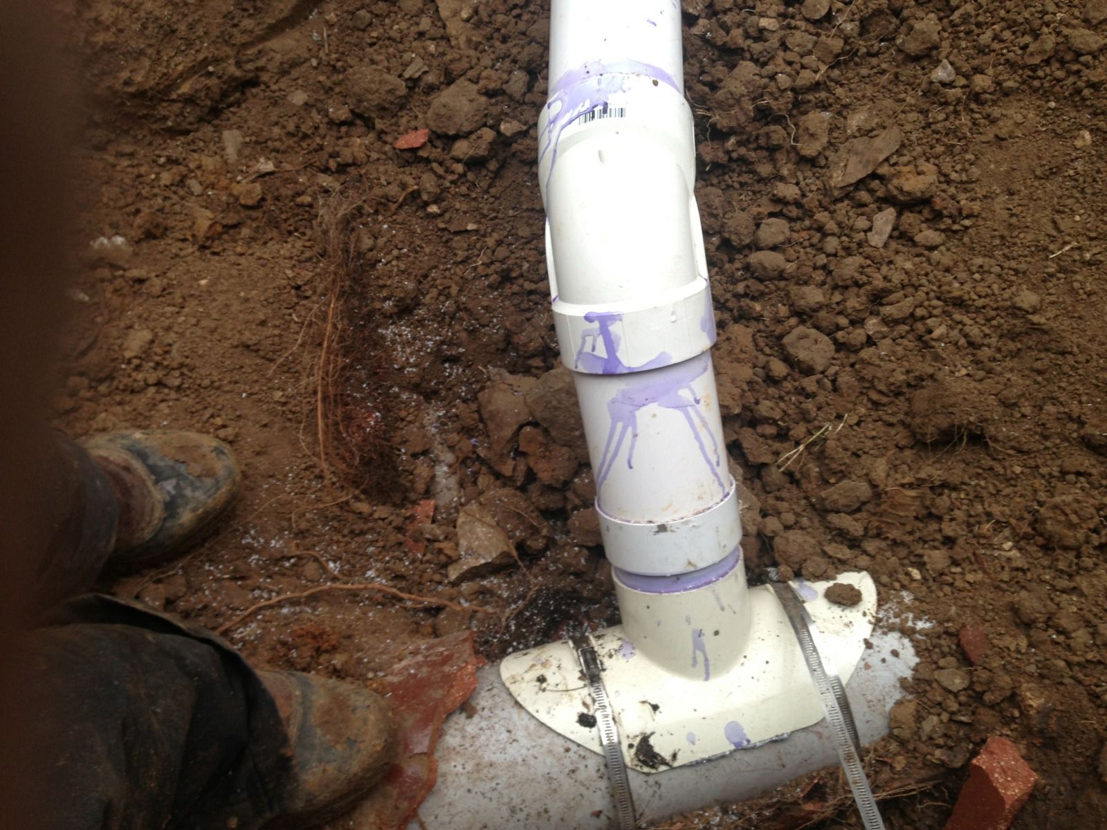 PVC pipes with purple glue, in a dirt trench.