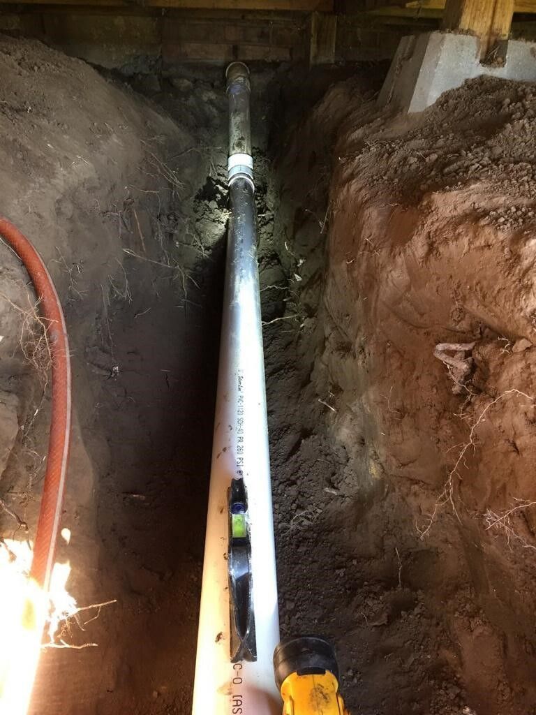 PVC pipe laid in a trench, being leveled with a bubble level in a construction site.