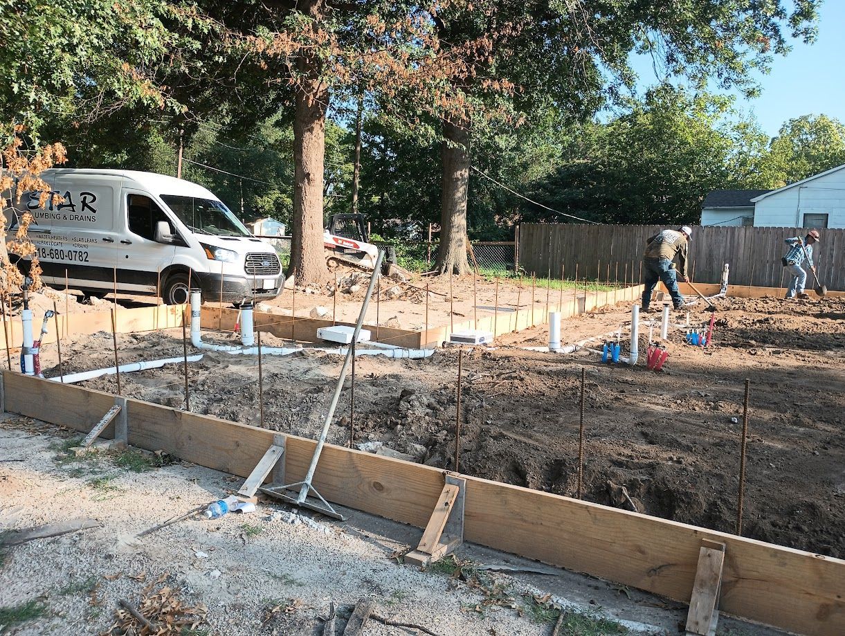 Construction site with wooden forms and pipes, van, and workers in backyard setting.