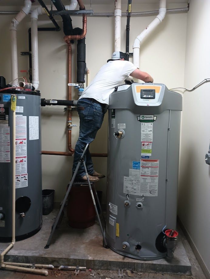 A person on a ladder working on a large water heater in a utility room.