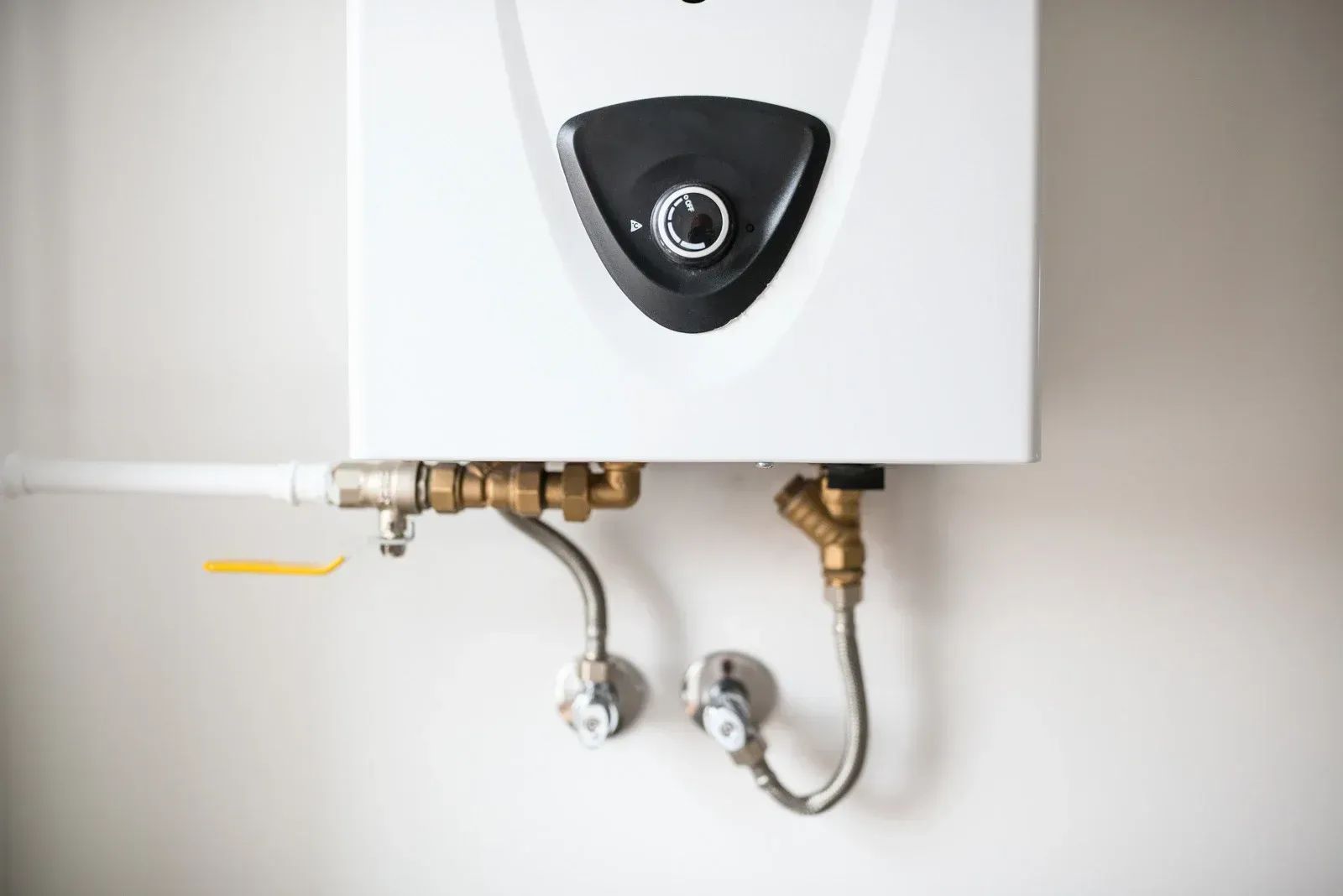 White tankless water heater mounted on a wall with copper pipes and valves.