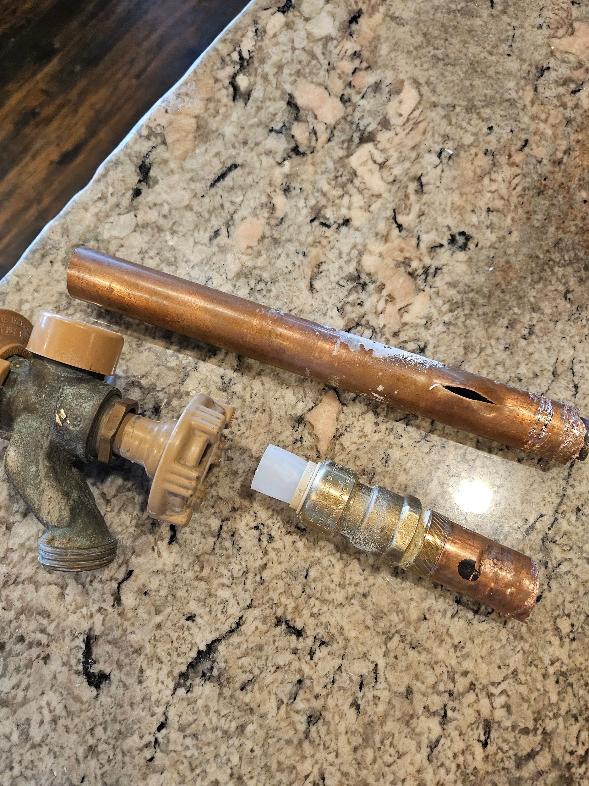 Broken outdoor faucet, copper pipe, and parts on a speckled countertop.