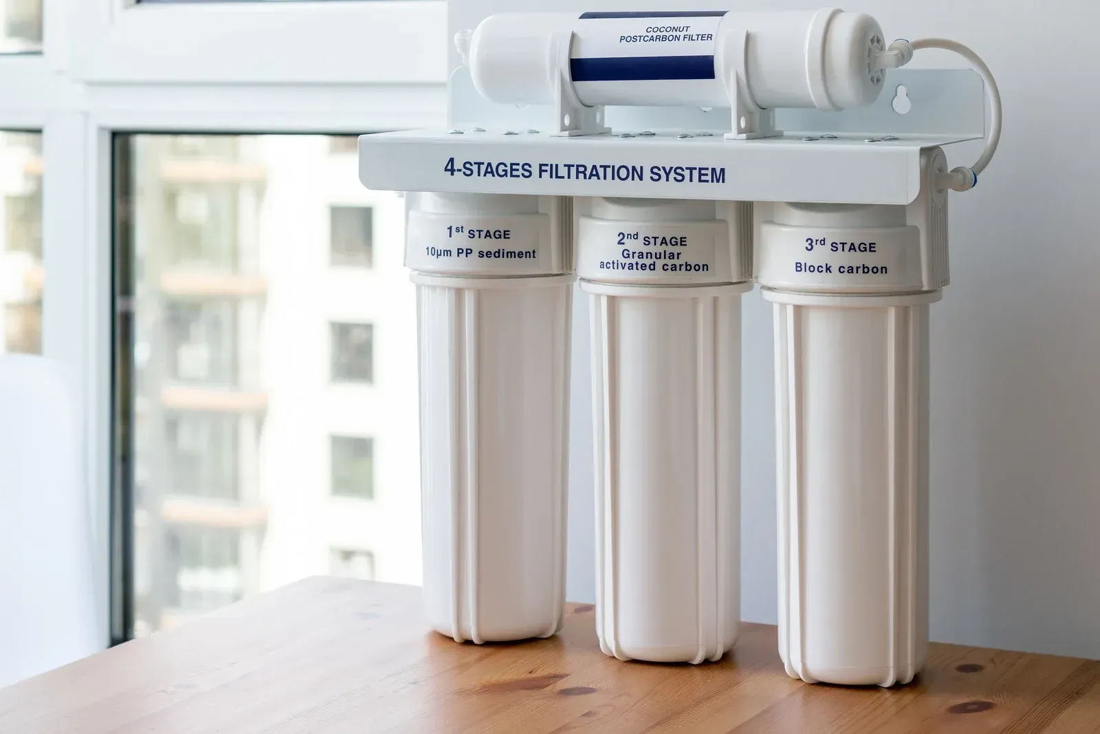 A four-stage water filtration system with three vertical white canisters and one horizontal filter on a wooden surface.
