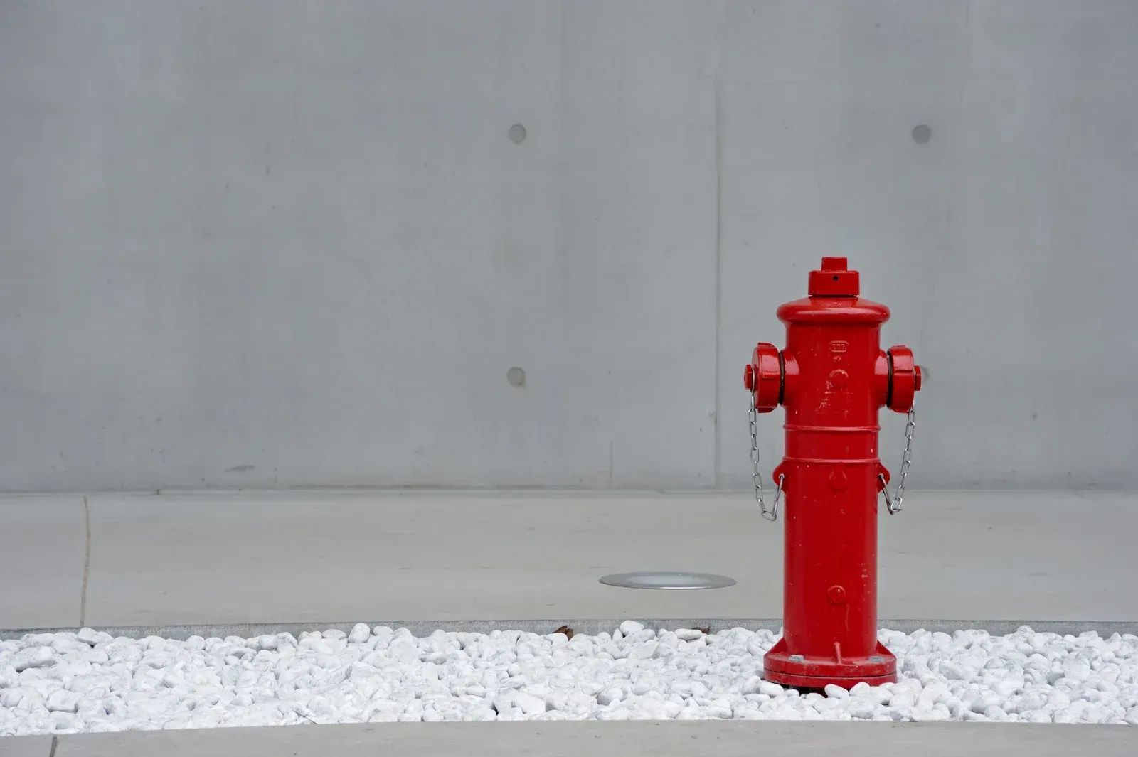 Red fire hydrant on white rocks in front of a gray concrete wall.