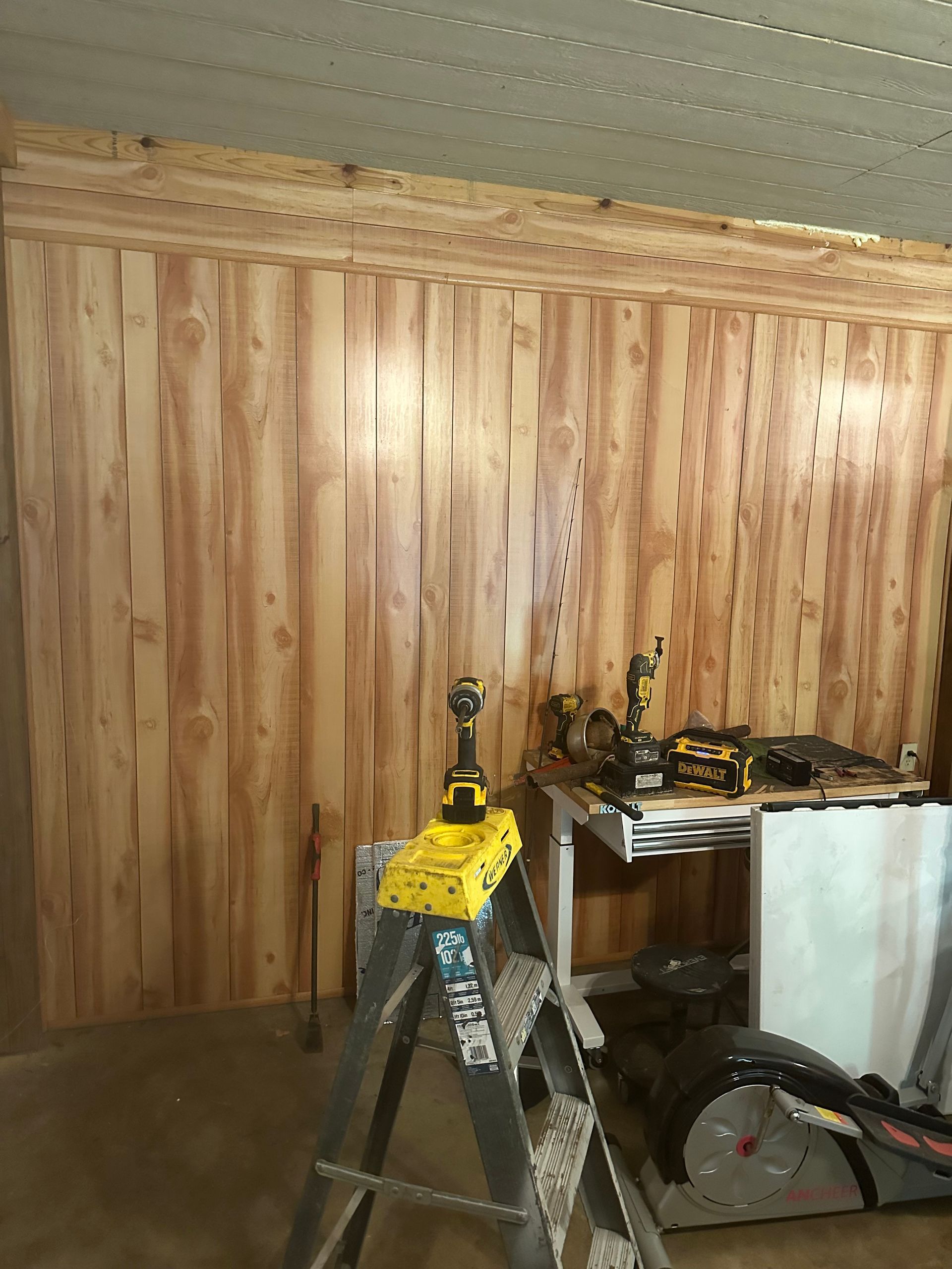 Wooden wall paneling in a workshop; ladder in foreground with tools on a table and wall.