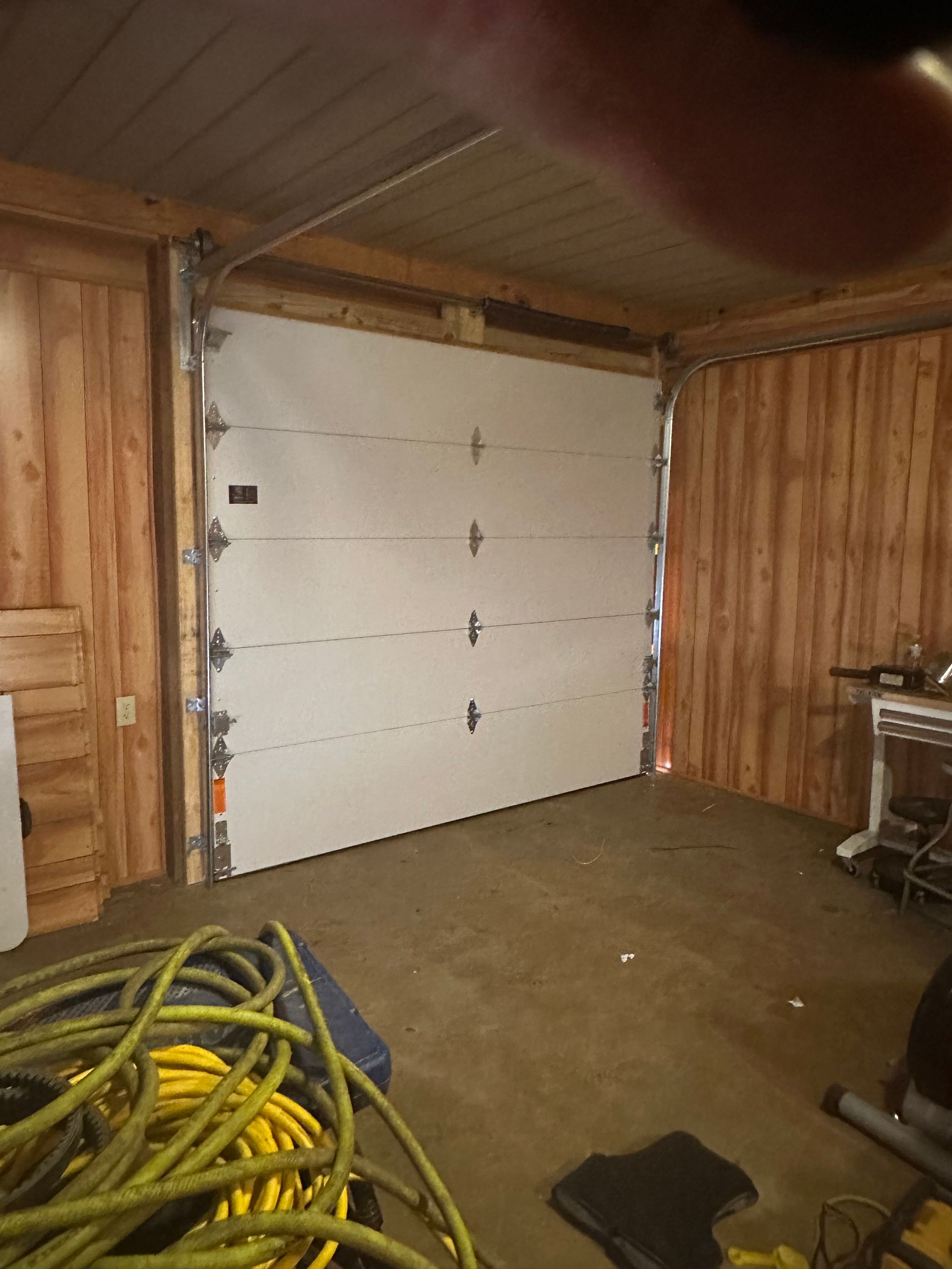Garage door closed inside a wooden structure; yellow hose on the floor.