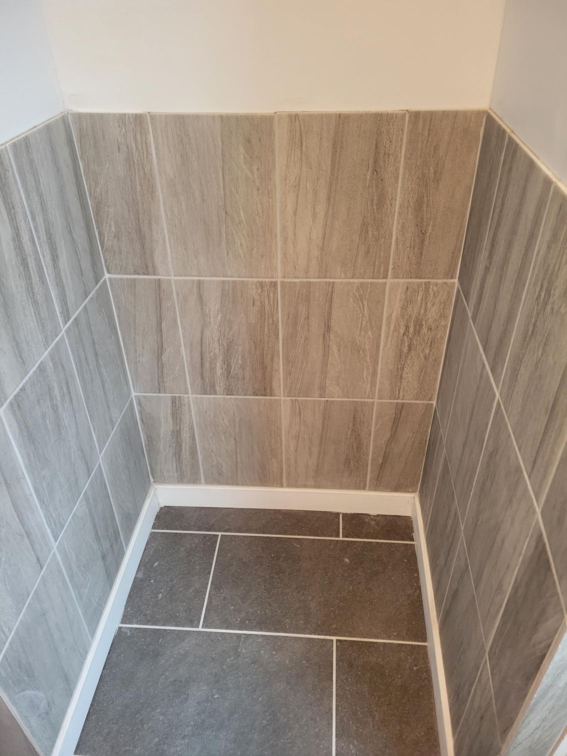 A corner of a bathroom with tiles on the wall and floor.