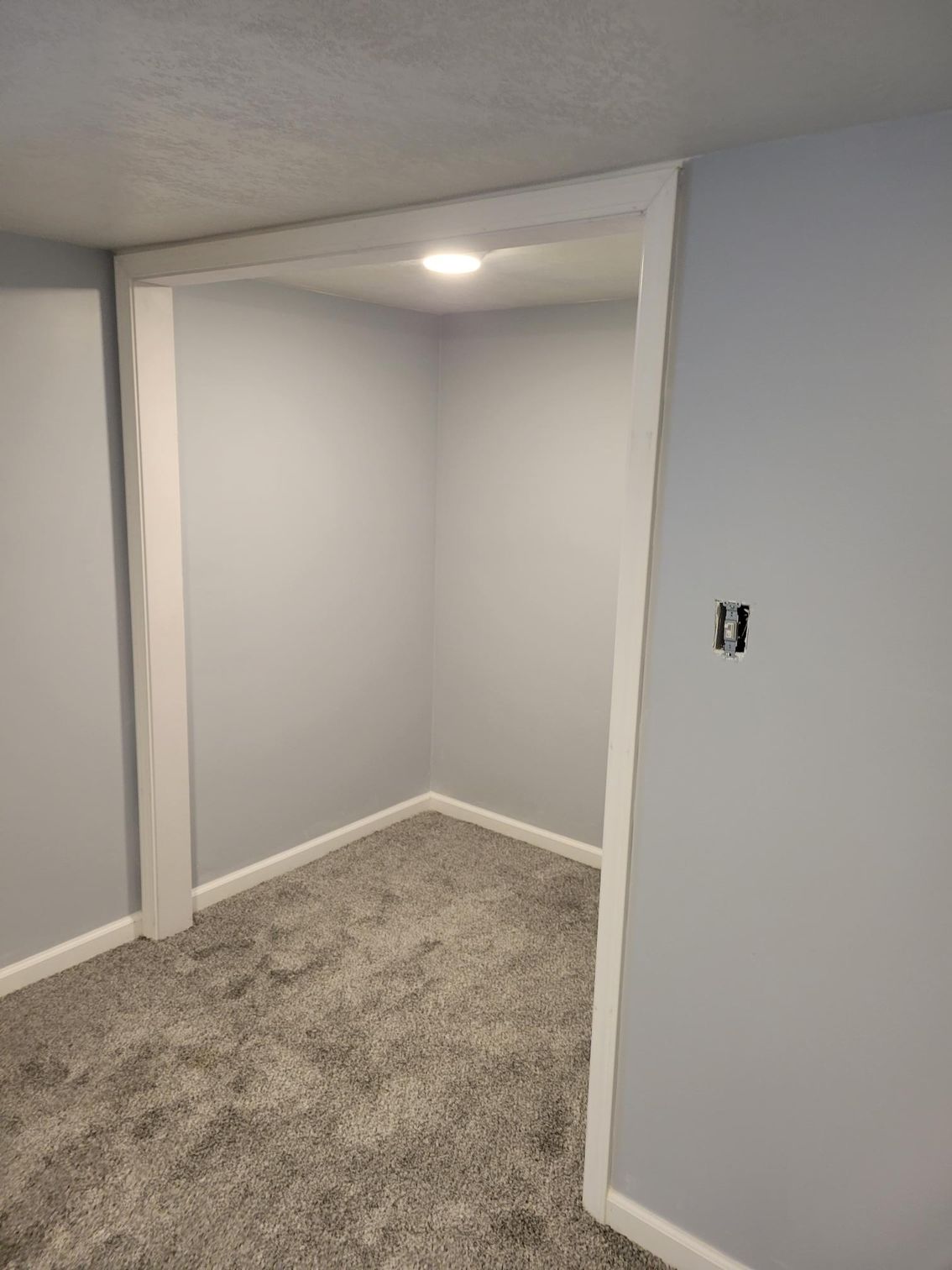 An empty room with a carpeted floor and gray walls.
