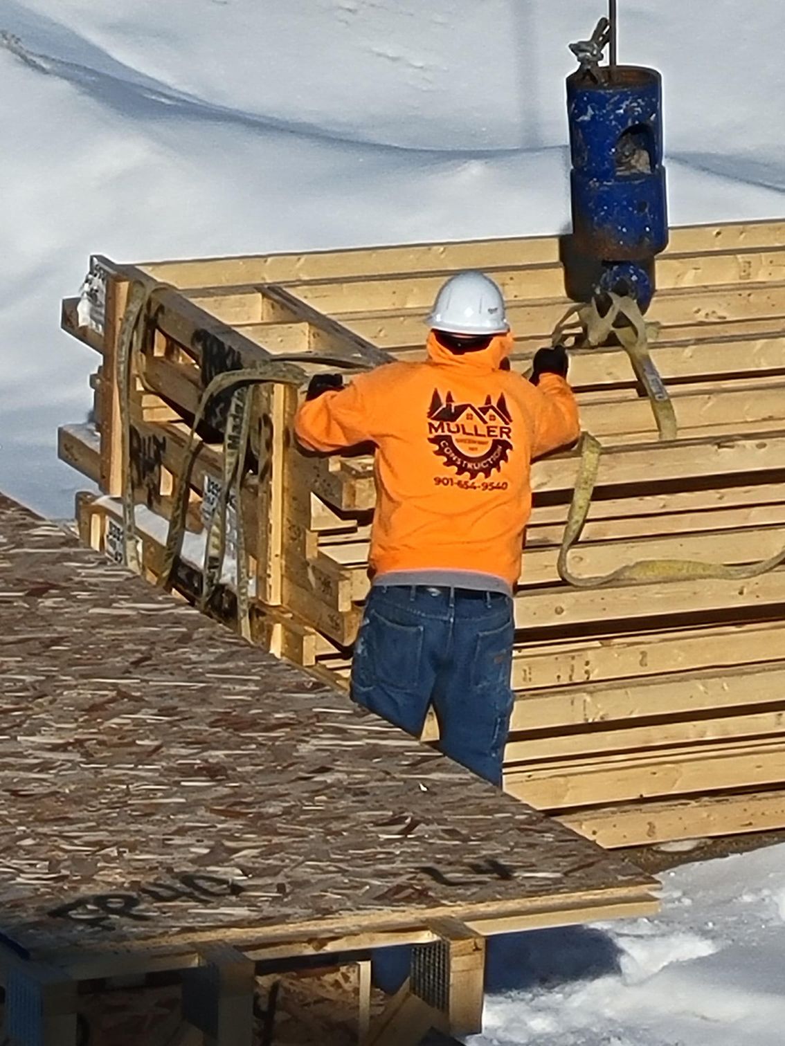 A man in an orange hoodie is lifting a wooden crate with a crane.