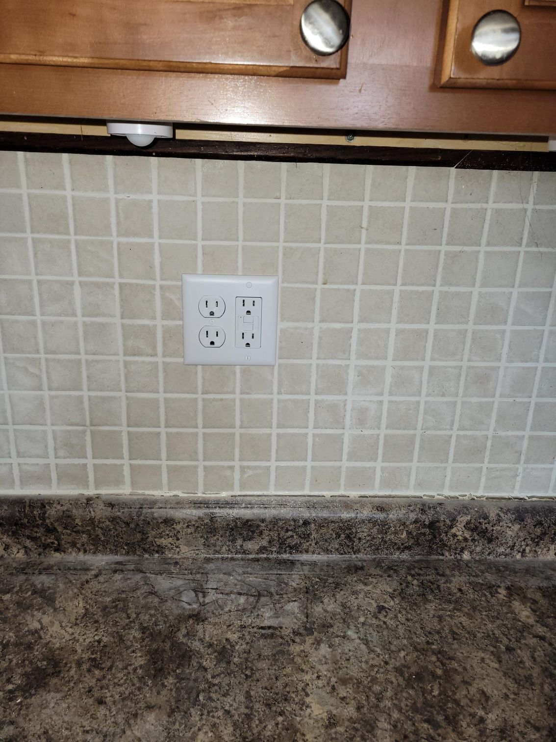 A kitchen counter with two electrical outlets on the wall.