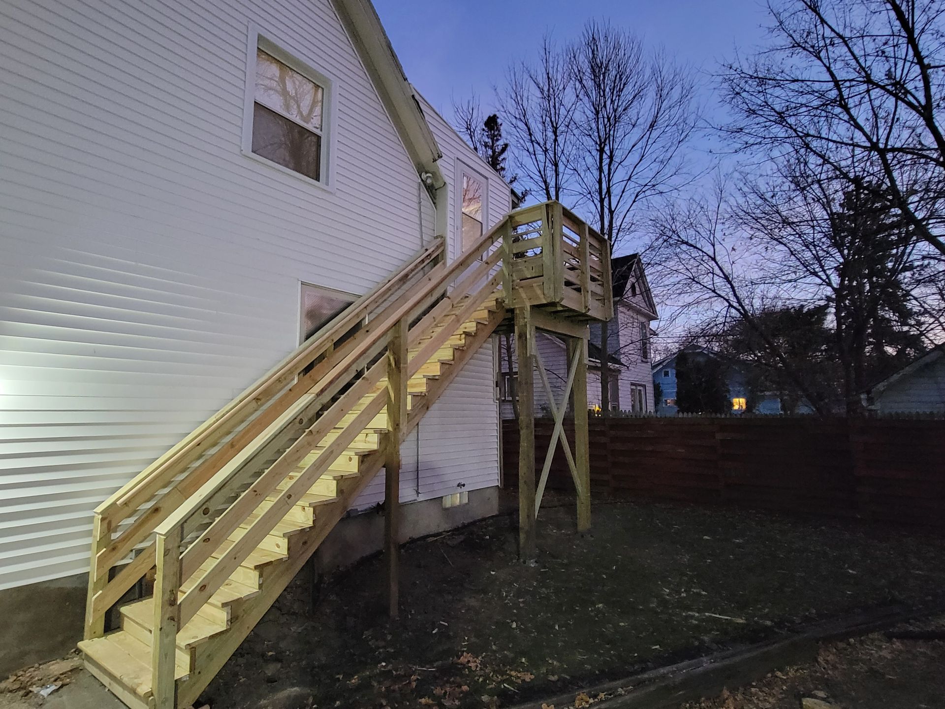 A white house with a wooden deck and stairs leading up to it.