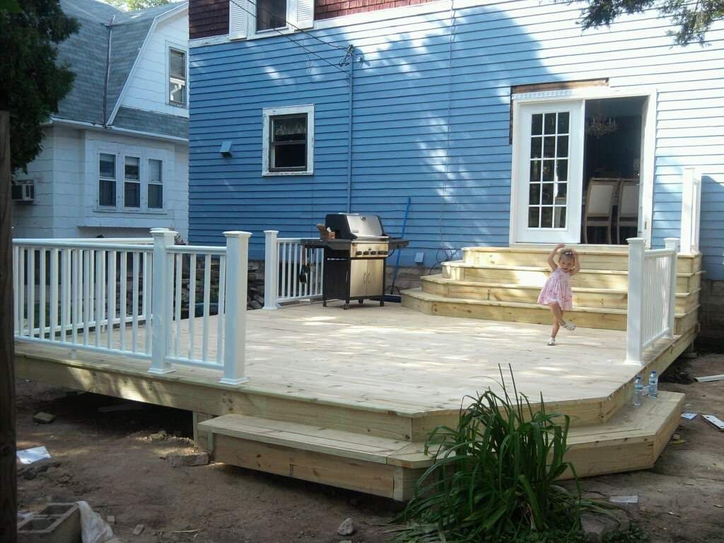A little girl is standing on a deck in front of a blue house