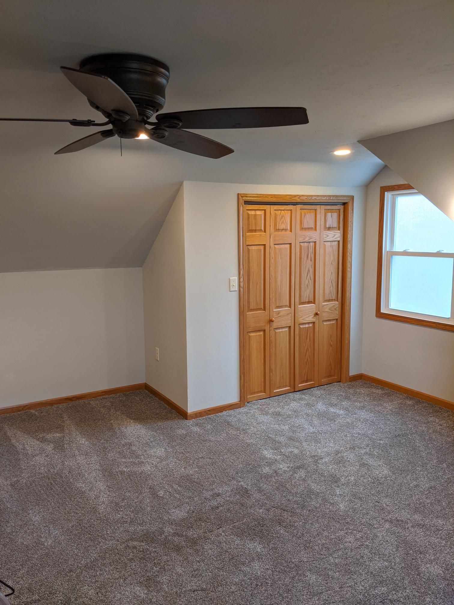 An empty bedroom with a ceiling fan and a window.