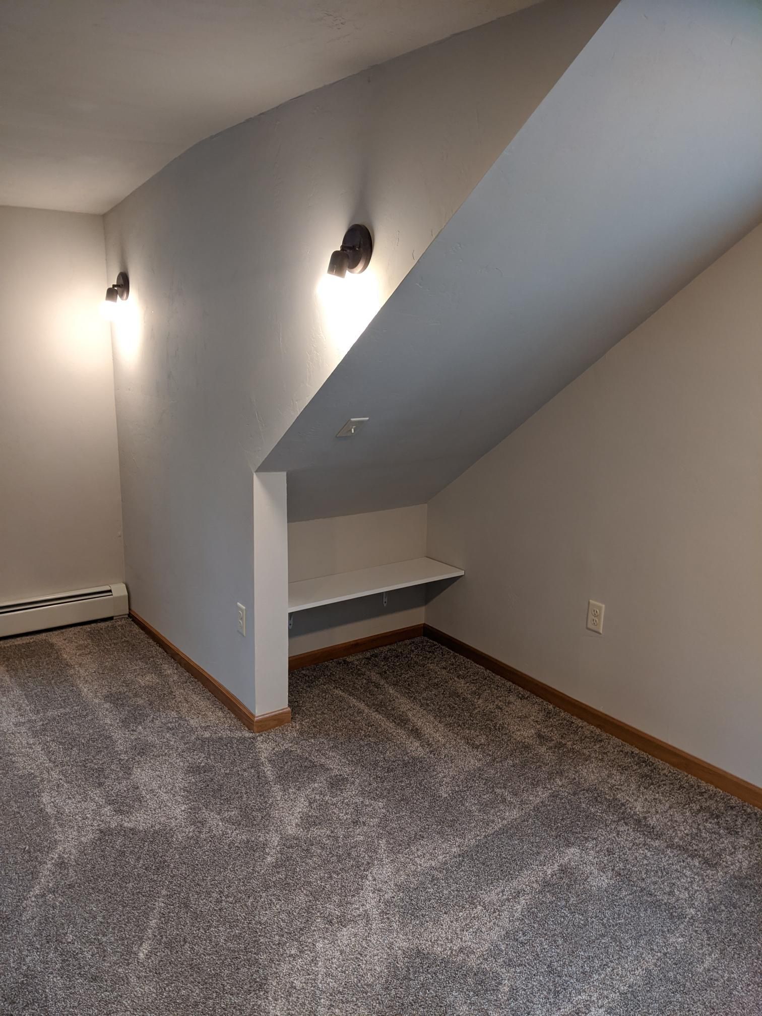An empty room with a staircase and a shelf in the corner.
