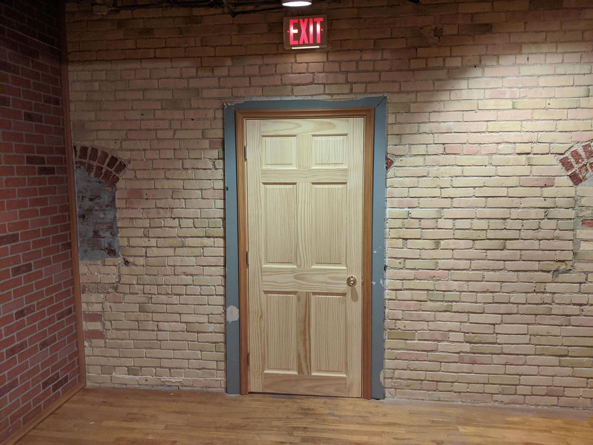 A brick wall with a wooden door and an exit sign above it
