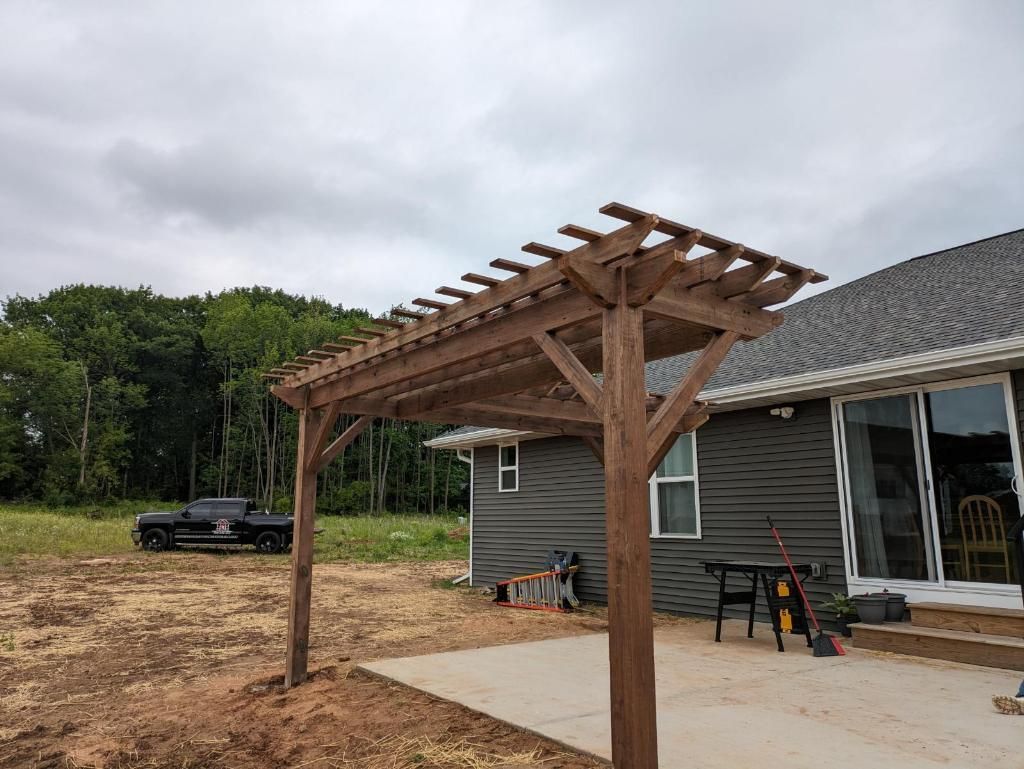 A wooden pergola is sitting in front of a house.