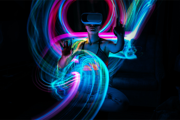 Woman wearing VR headset, illuminated by colorful light streaks, interacting with a virtual environment in the dark.
