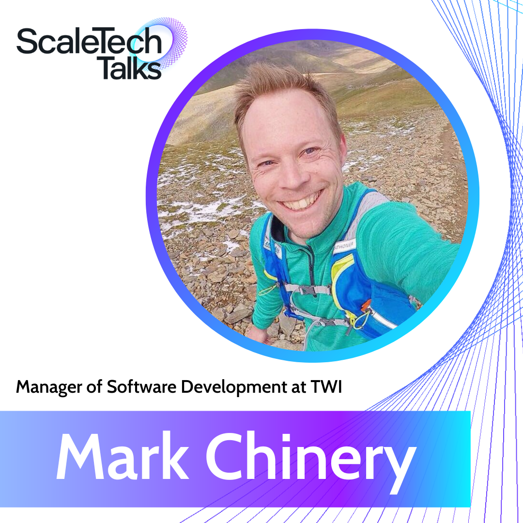Mark Chinery, Manager of Software Development, smiles outdoors. He wears a teal shirt and a blue hydration pack.
