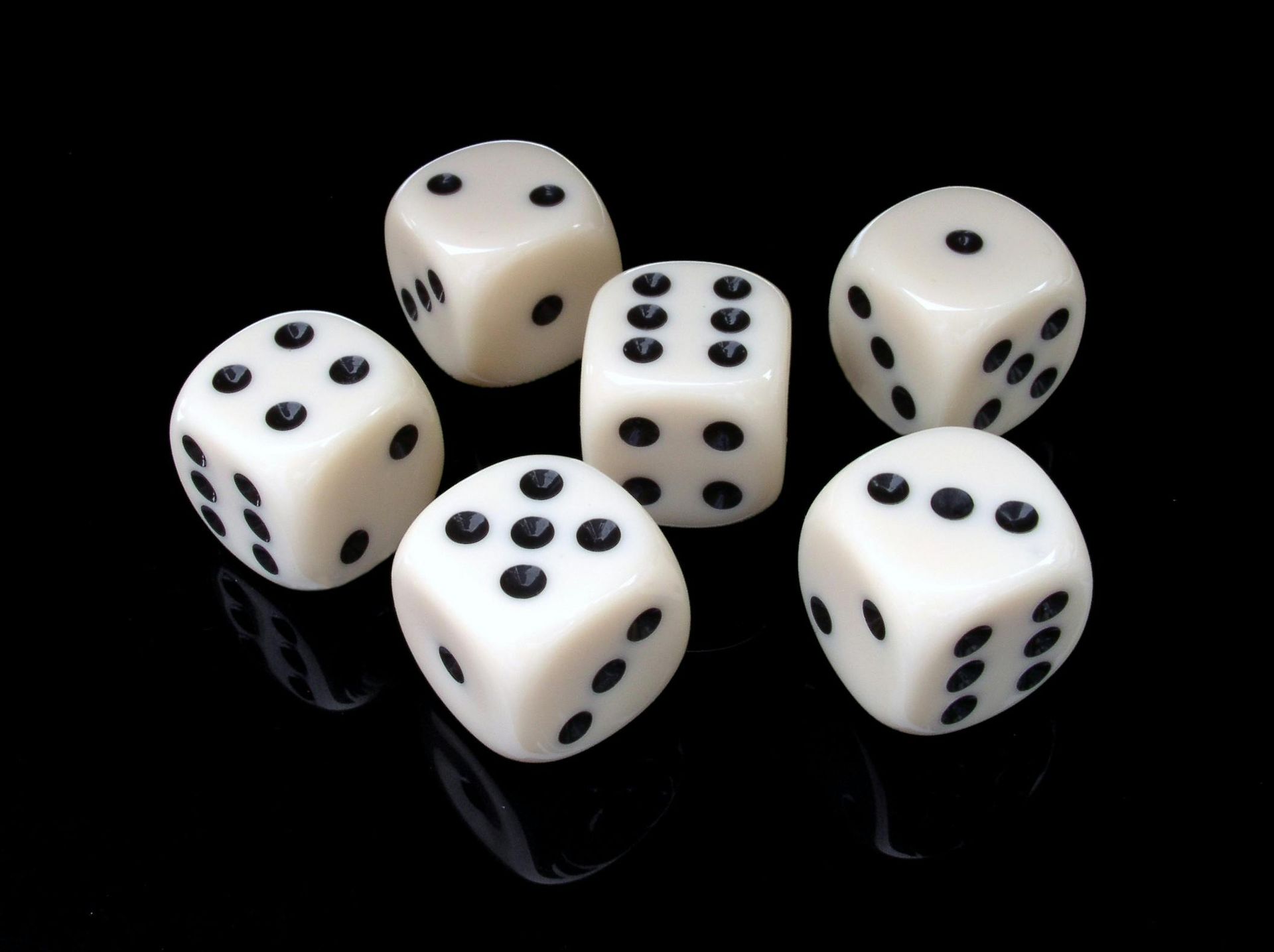 Six white dice with black dots, scattered on a black surface.