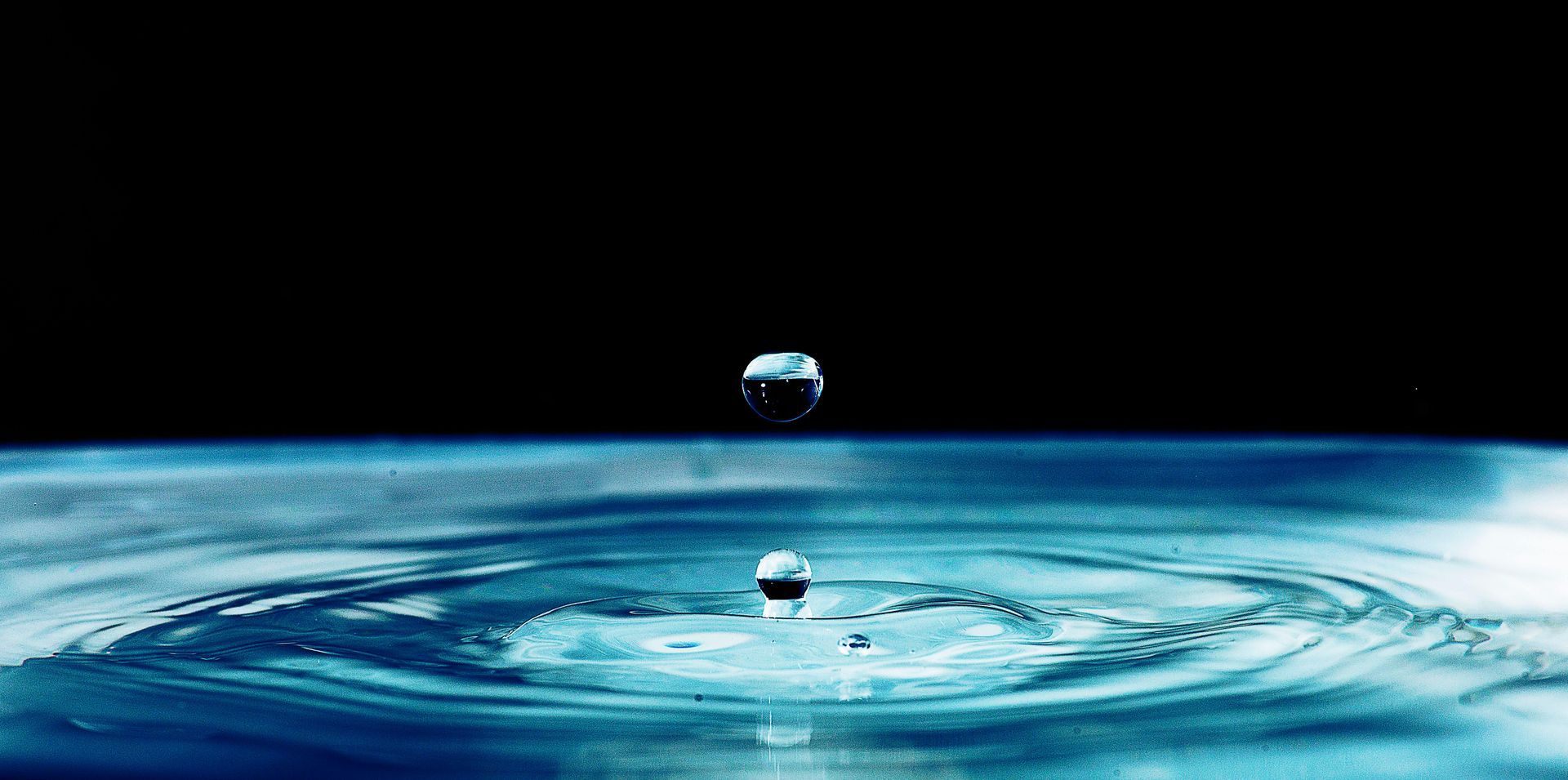 Water droplet falling into water, creating ripples. Black background.