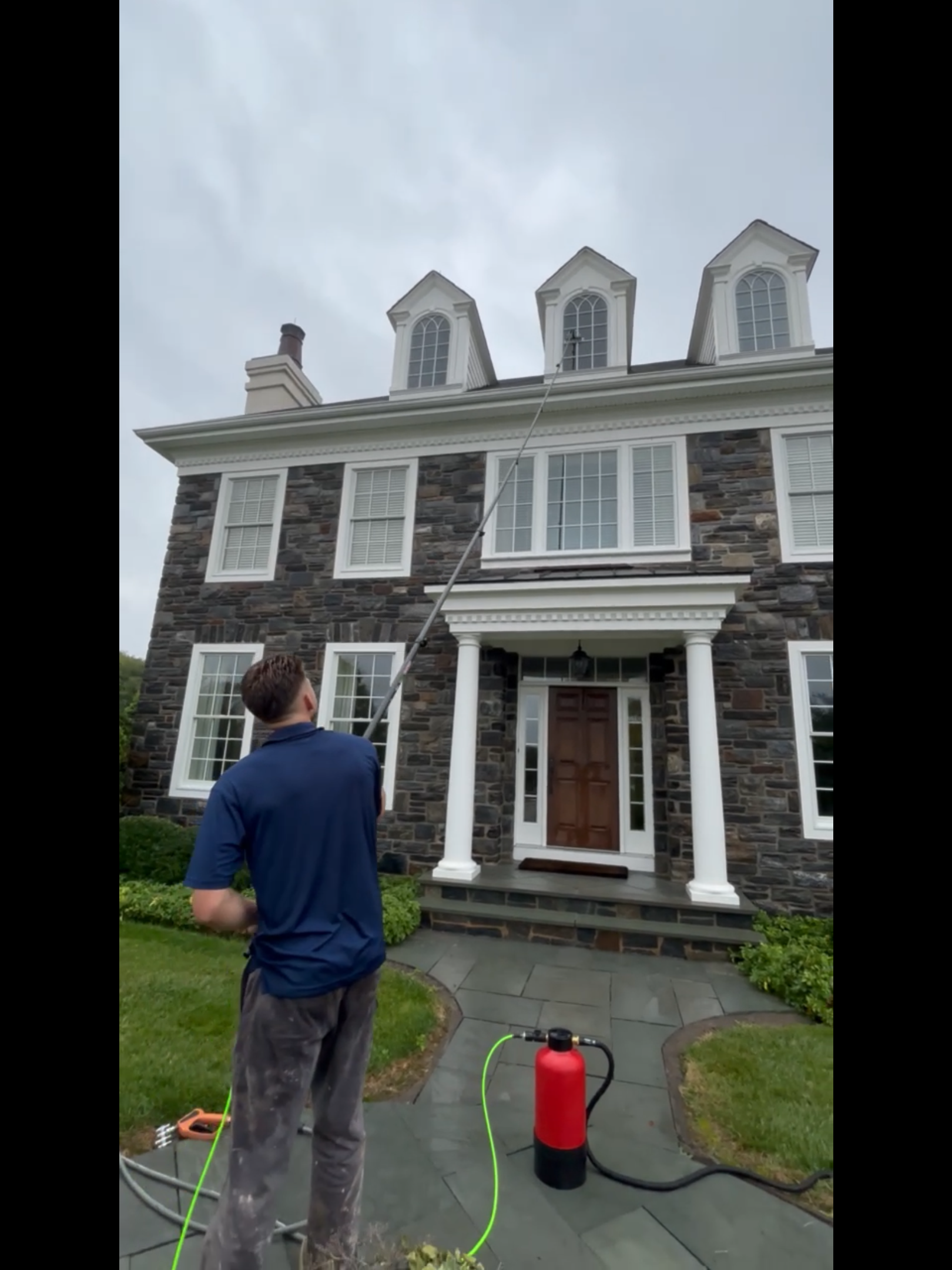 A man is cleaning a large stone house with a pressure washer.