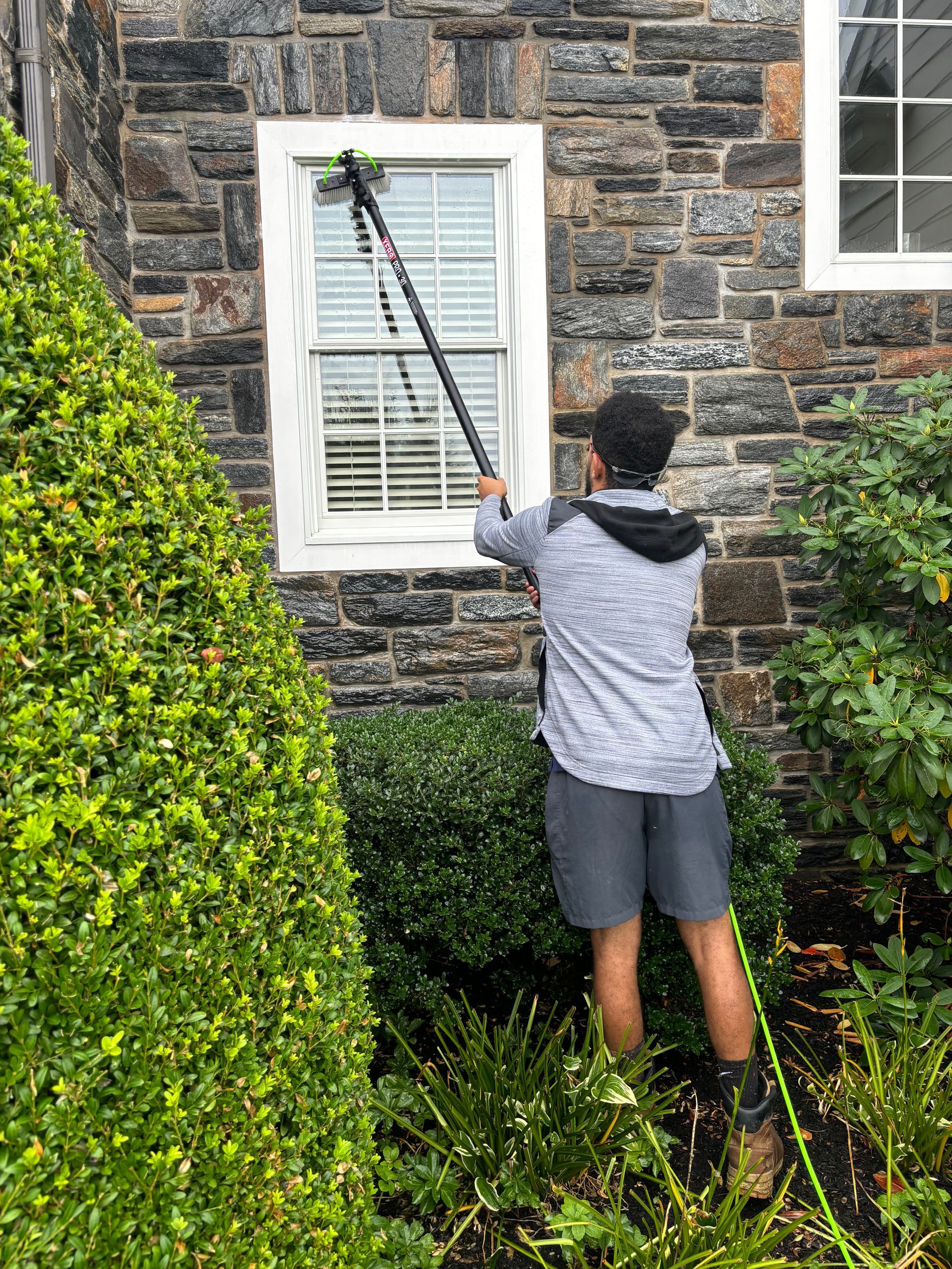 A man is cleaning a window with a hose on a stone wall.