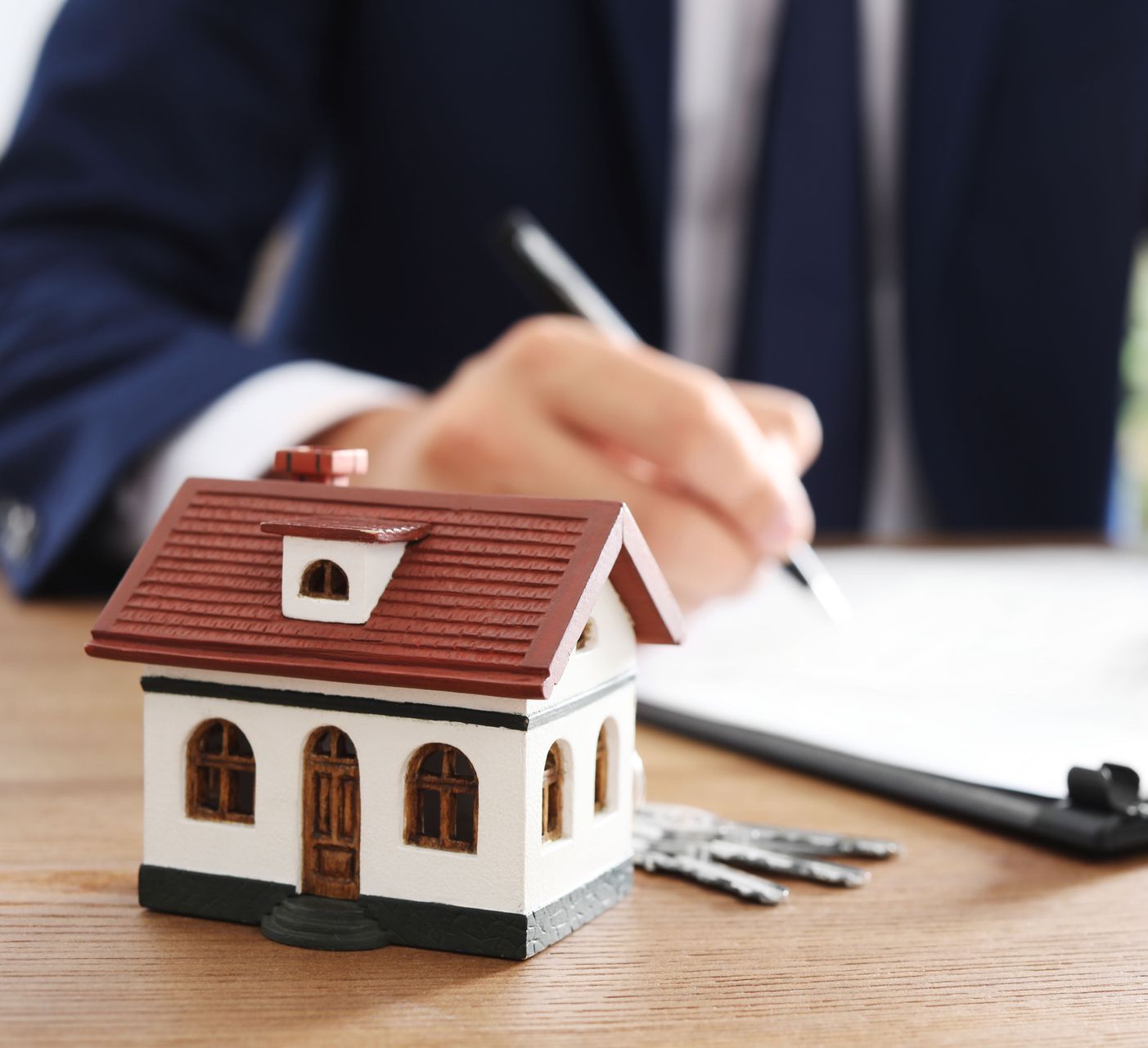 A man is writing on a clipboard next to a model house