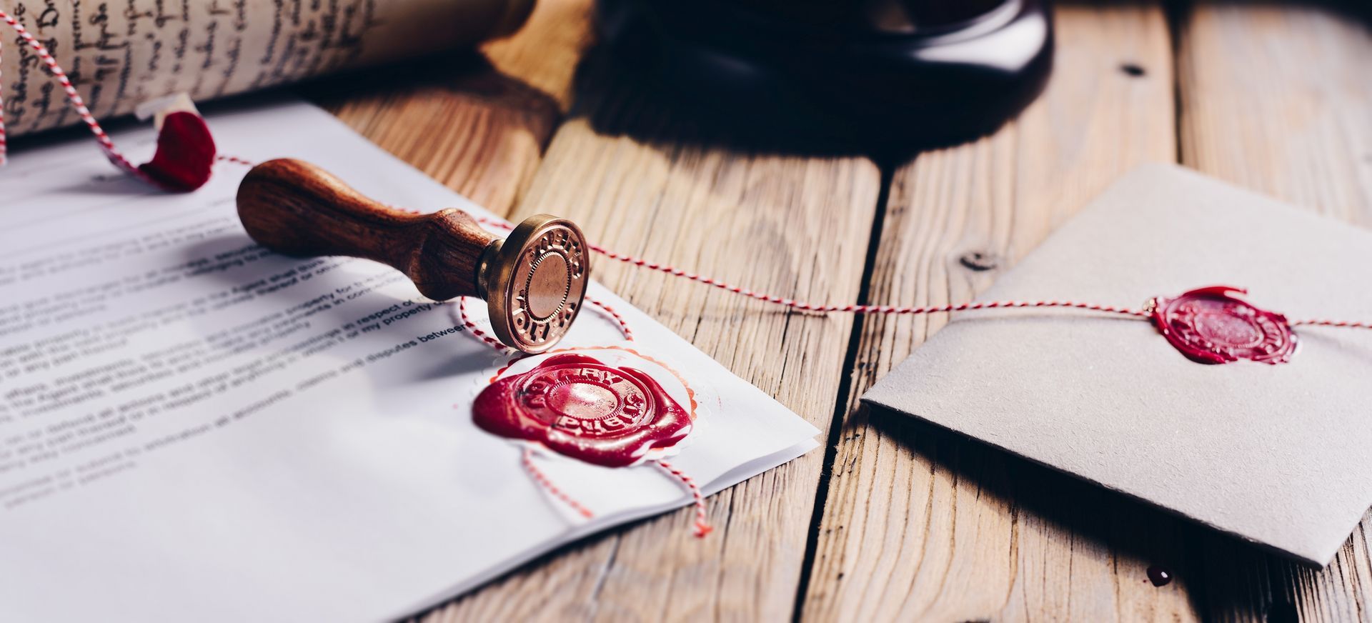Wax-sealed invitation envelopes and a stamp on a wooden table with pink cord