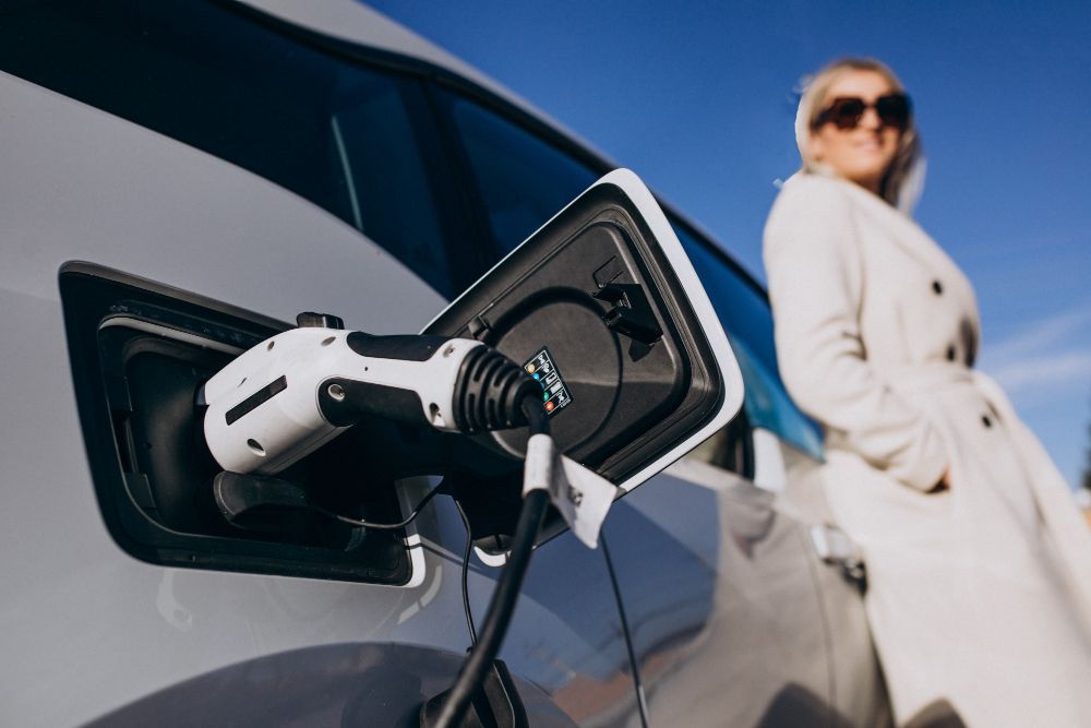 A woman is standing next to an electric car that is being charged.