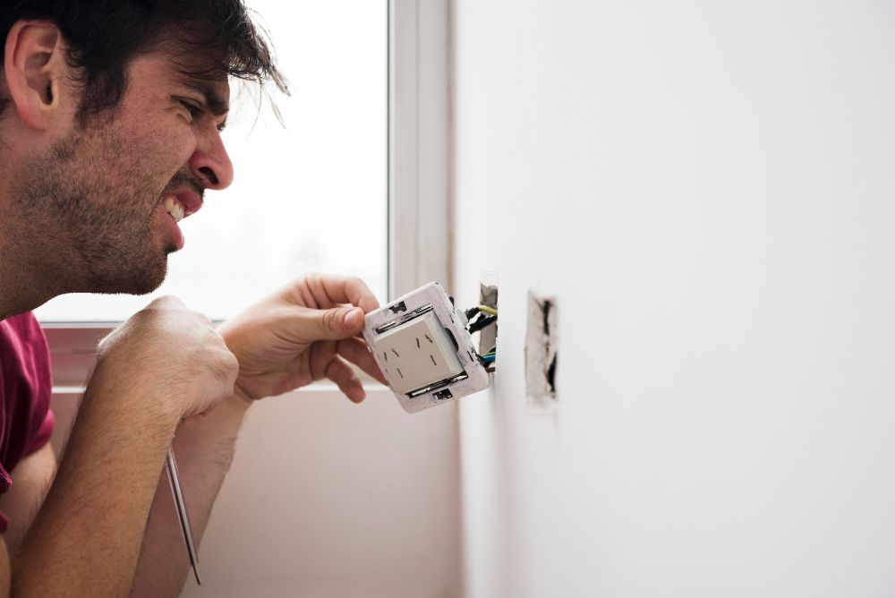 A man is fixing an electrical outlet on a wall.