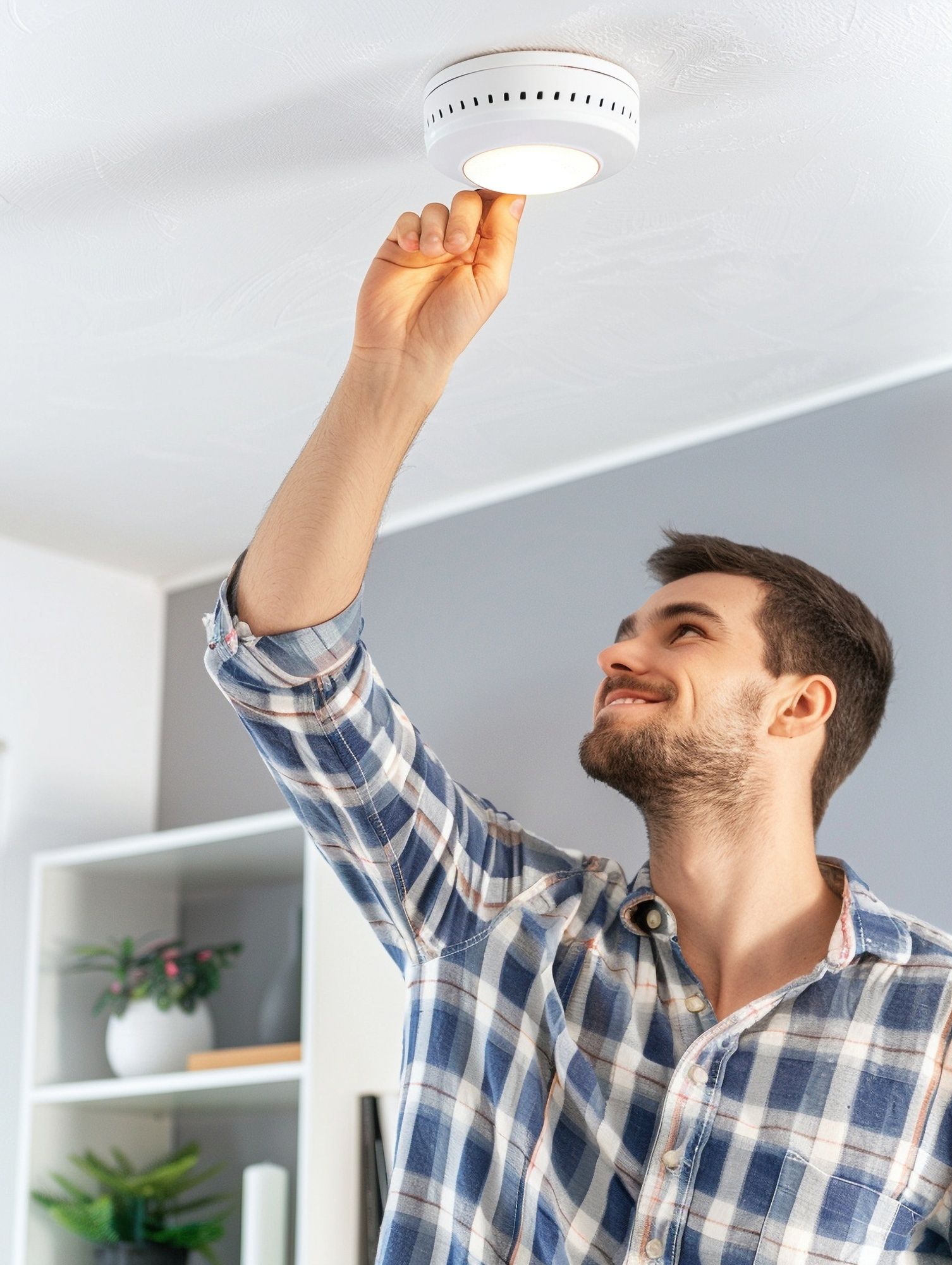 A man is installing a smoke detector on the ceiling.