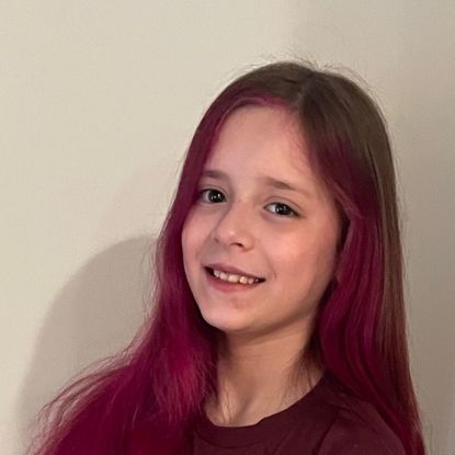 A young girl with purple hair is smiling for the camera.
