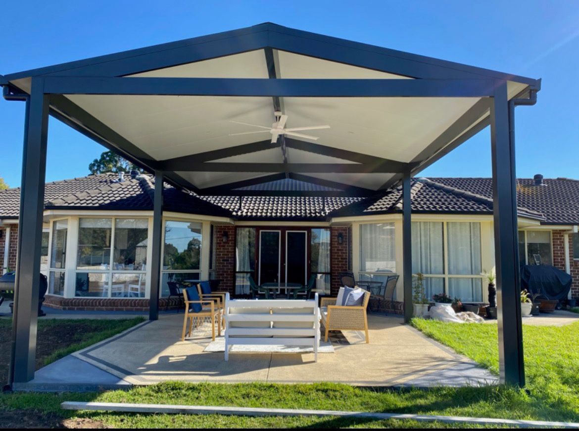 A patio with a roof and a table and chairs underneath it in front of a house  | Berkshire Park, NSW | V.J.S. Aluminium & Steel