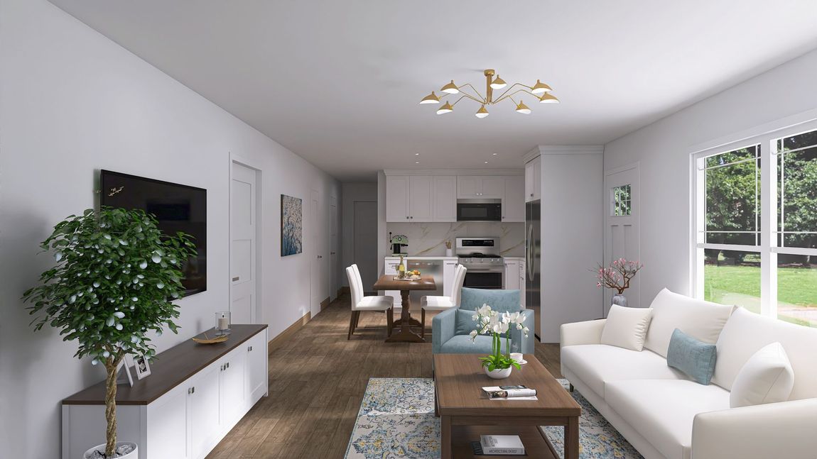 Living room with white walls, kitchen in the back, white sofa, wooden floor, and a large window looking outside.