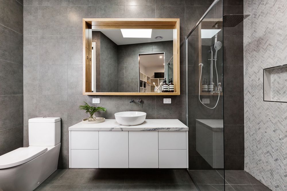 Bagno moderno grigio con doppio lavabo, lavabo rotondo, ampio specchio, doccia in vetro e WC bianco.