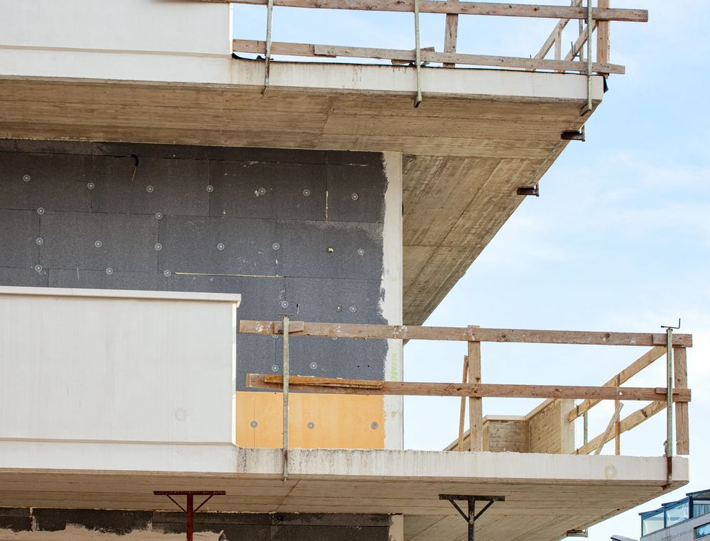 Edificio in cemento parzialmente costruito con impalcature e pareti esterne non rifinite sotto un cielo azzurro.