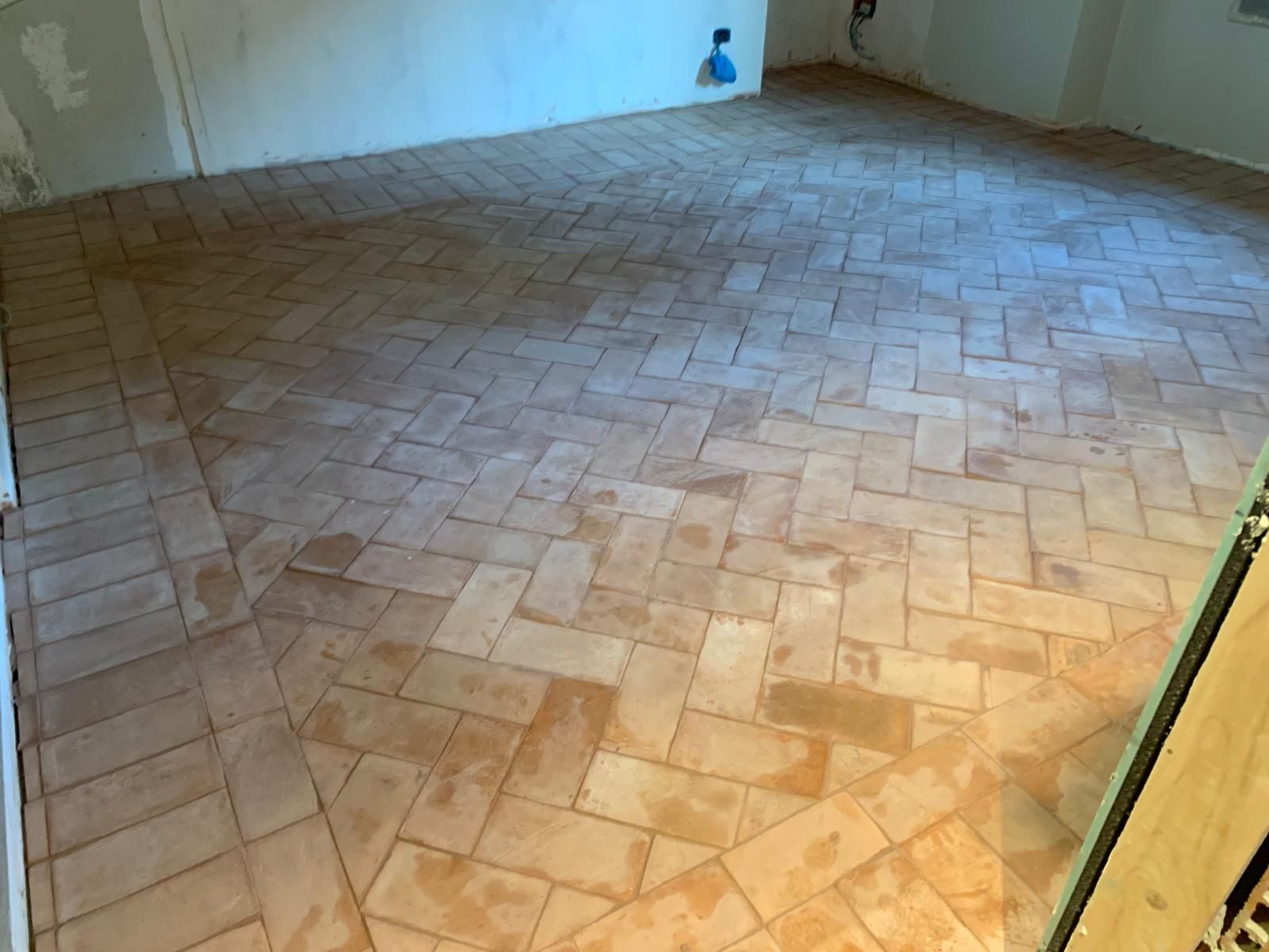 Stanza vuota con pavimento piastrellato beige e pareti bianche, vista da una porta.