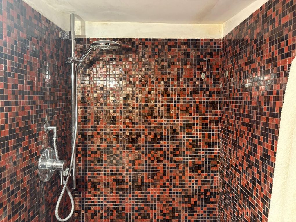 Cabina doccia con pareti rivestite in piastrelle a mosaico rosse e nere e soffione cromato.