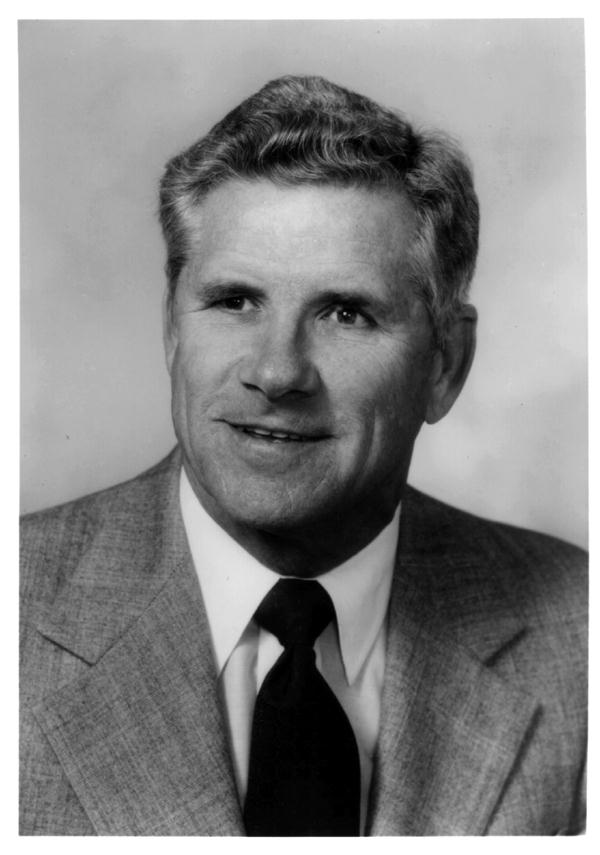 A man in a suit and tie is smiling in a black and white photo.
