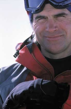 A man wearing a red jacket and goggles is smiling for the camera.